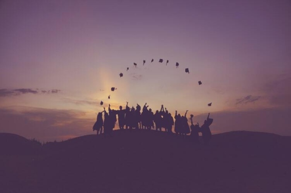 There is a sunset and a group of graduates who are throwing their graduation caps into the air.